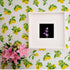 A framed print of a detailed purple sage flower against a black background, displayed on a lemon-patterned wallpaper, complementing the floral aesthetic.