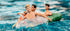 Three vintage New Kids on the Block dolls floating on inflatable pool rings in splashing blue water, with bright summer lighting and playful retro vibes